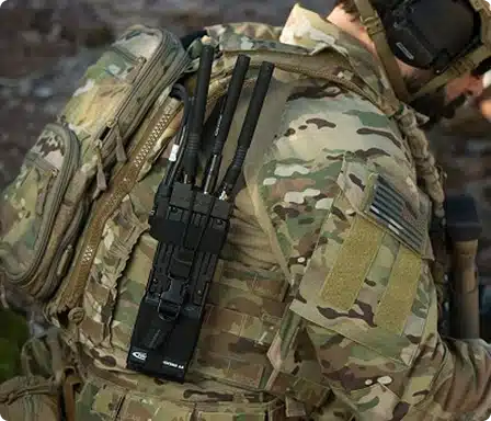 Soldier carrying backpack-mounted tactical RF radios with clustered whip antennas for field ops